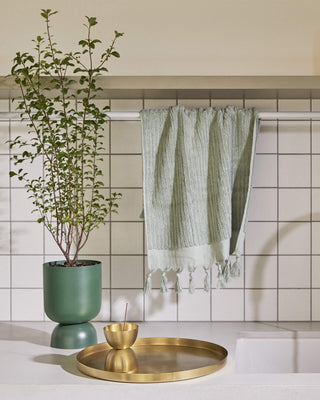 Green goblet planter with juniper, brass tray, and towel