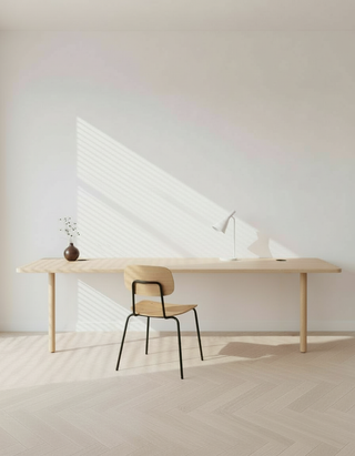 Minimalist desk setup with a chair and lamp in a room with white walls and wooden floor.
